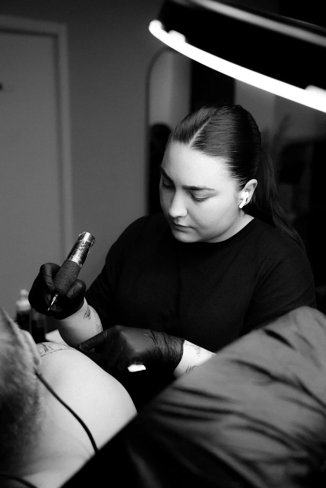 Alba tatuando en su estudio, retrato en blanco y negro con la máquina rotativa en la mano y la luz de aro de fondo