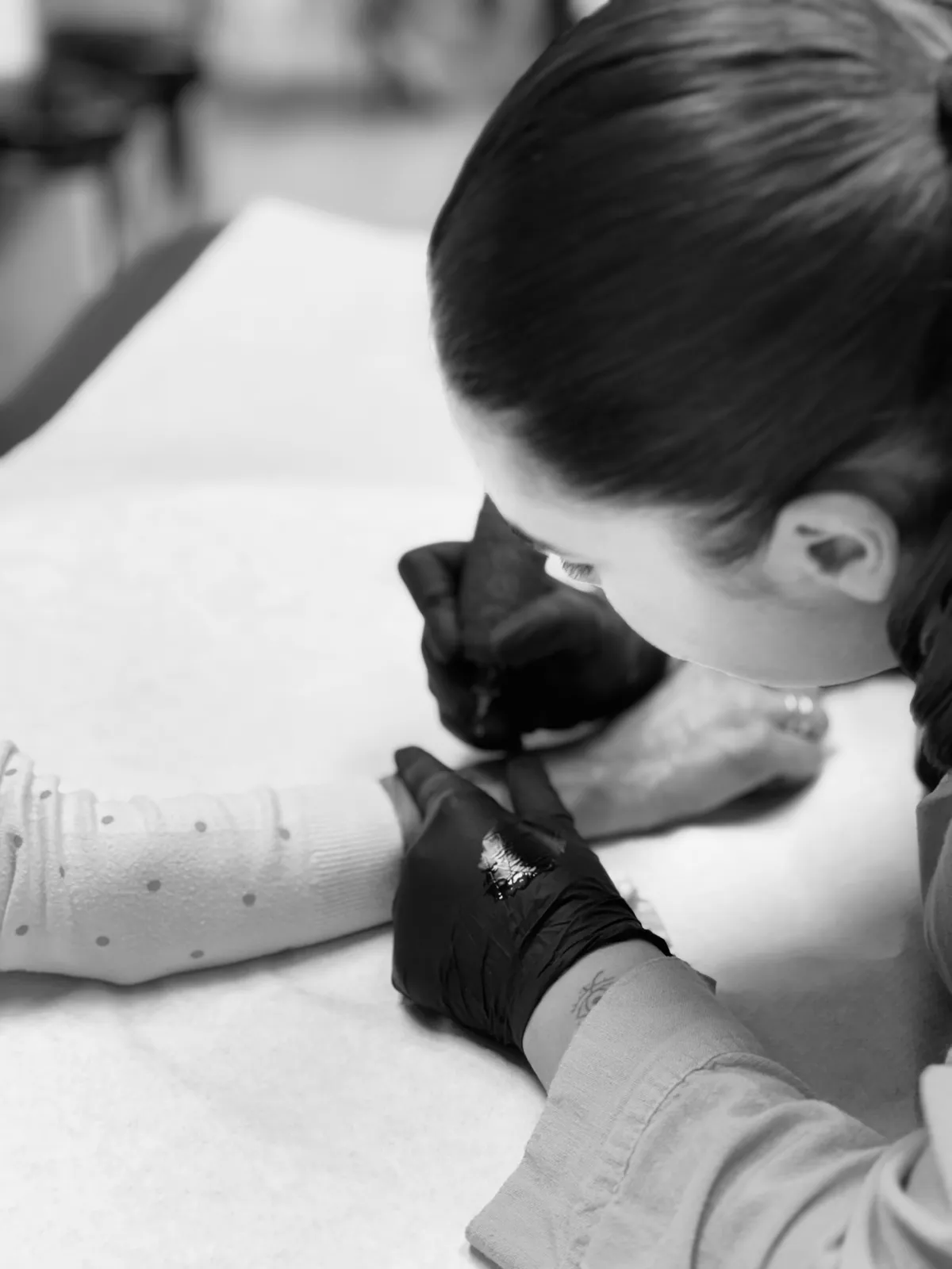 Alba concentrada tatuando un antebrazo, fotografía en blanco y negro con guantes negros y toalla blanca