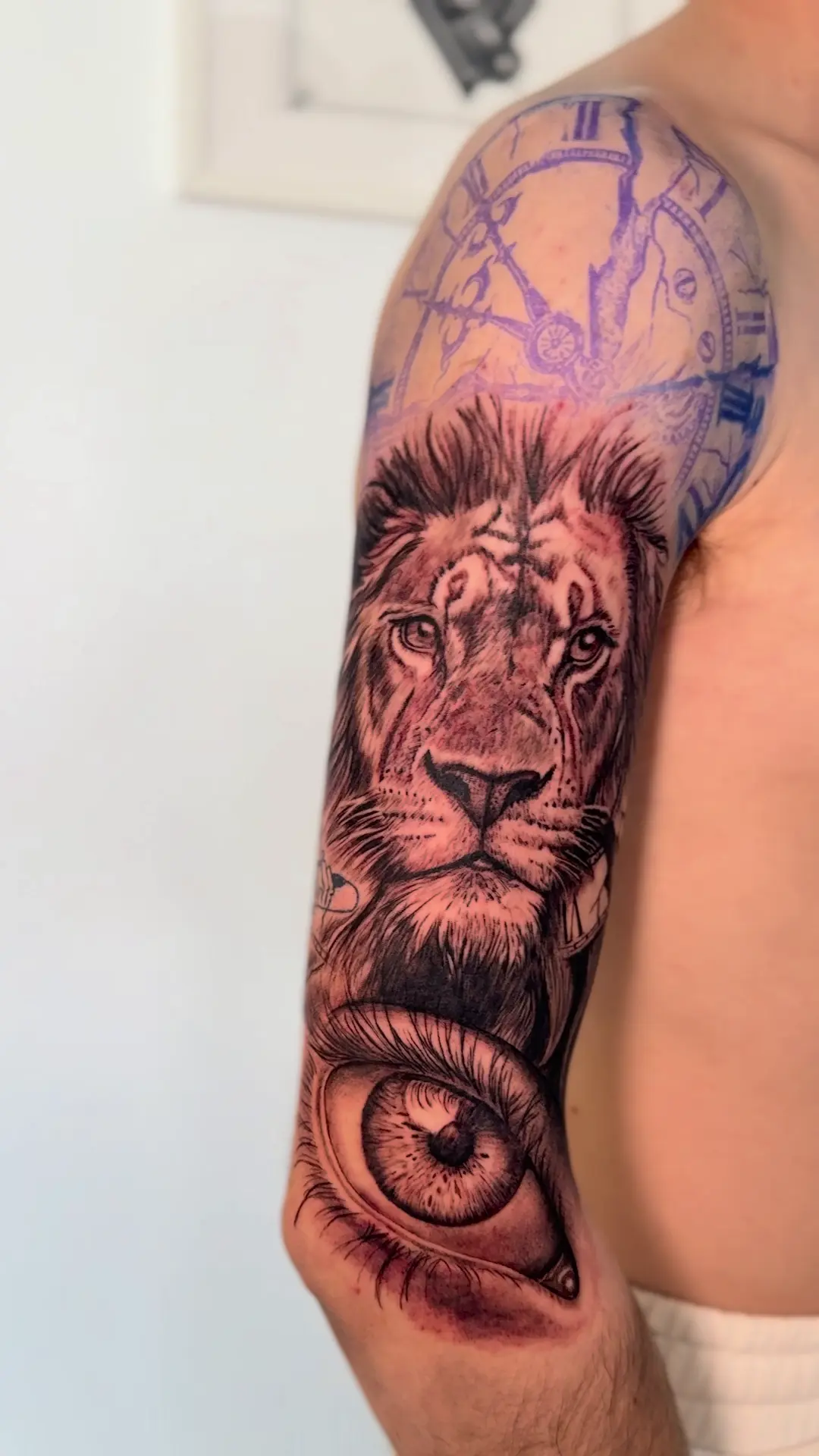 Medio brazo con un león en realismo y un ojo hiperrealista, con el stencil del reloj todavía marcado