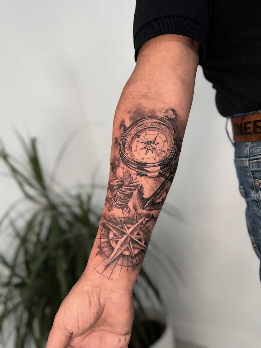Brújula antigua, ancla y rosa de los vientos tatuadas en realismo negro y gris en todo el antebrazo