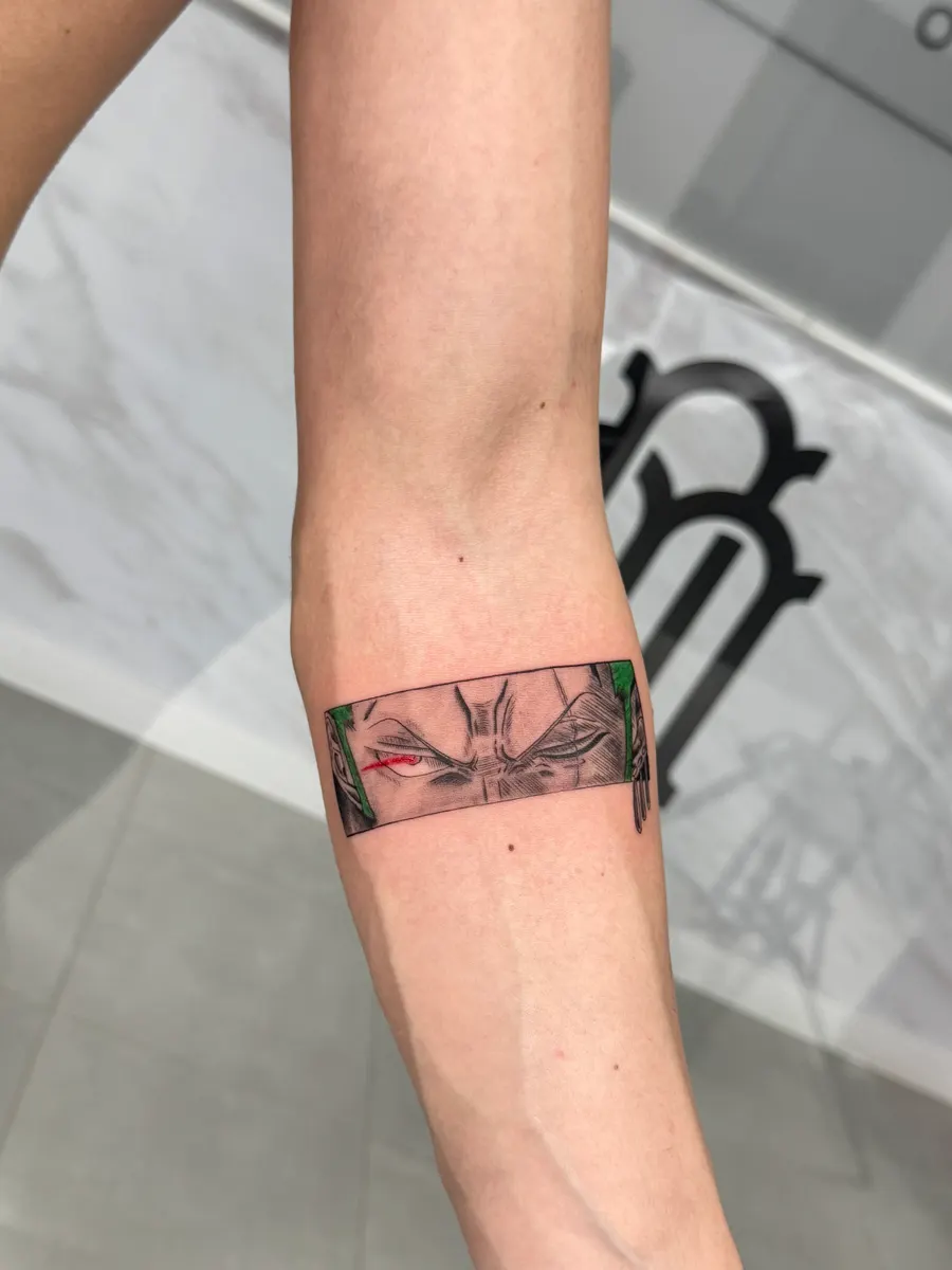 Brazalete tatuado en el antebrazo con la mirada de un personaje de anime y un acento en verde y rojo