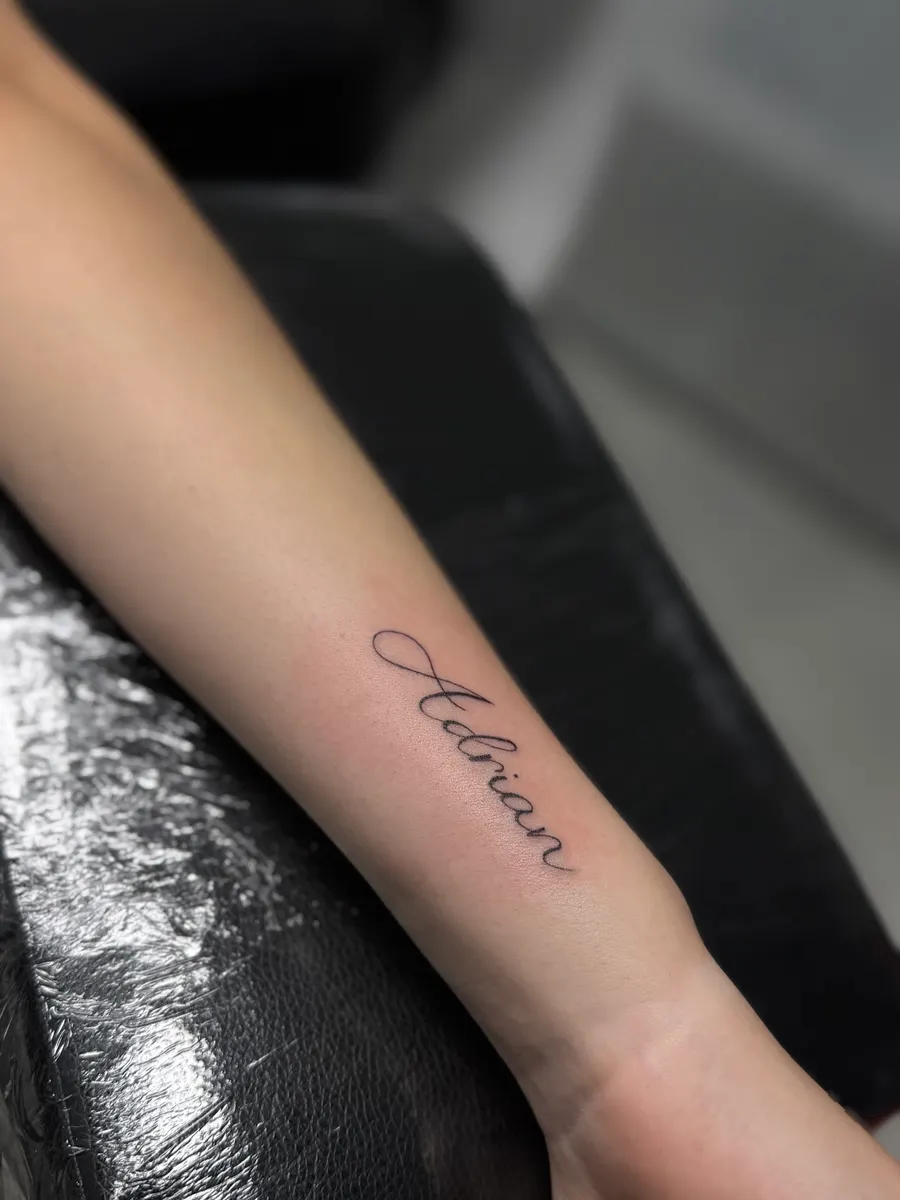 Nombre Adrian tatuado en lettering cursivo de trazo fino en el antebrazo